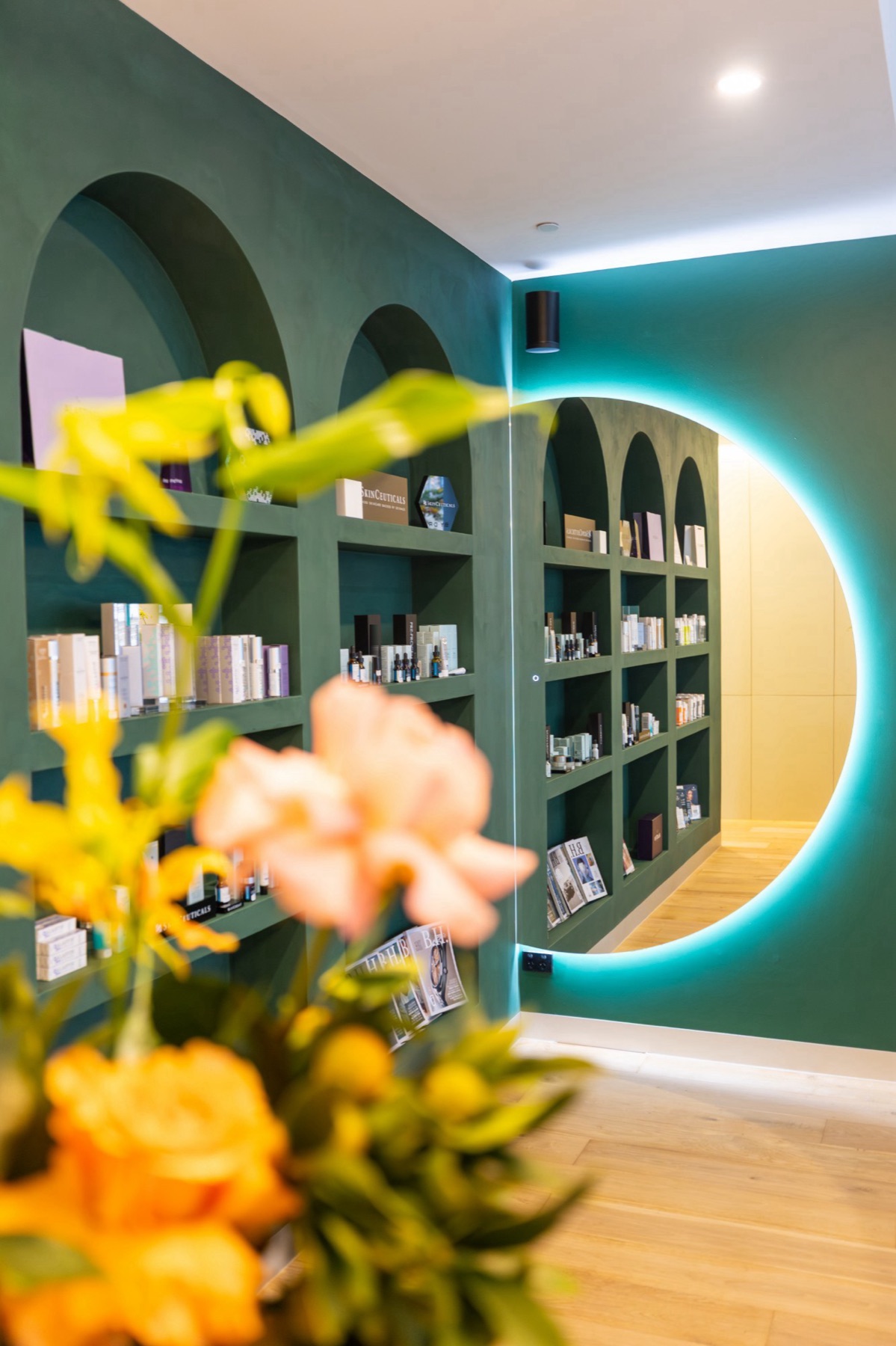 Cleon's retail room in Potts Point: green arched skincare shelves and a softly lit round mirror, with flowers in the foreground