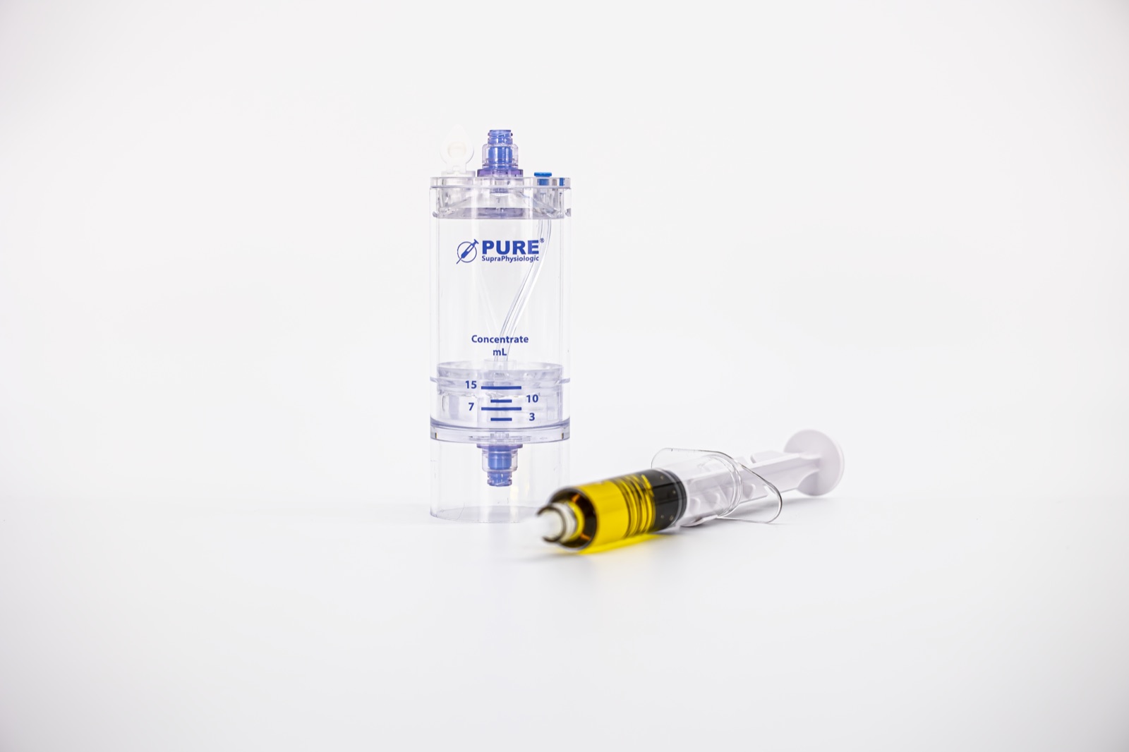 A syringe of golden PurePRP resting in front of the clear EmCyte concentrator it was drawn from