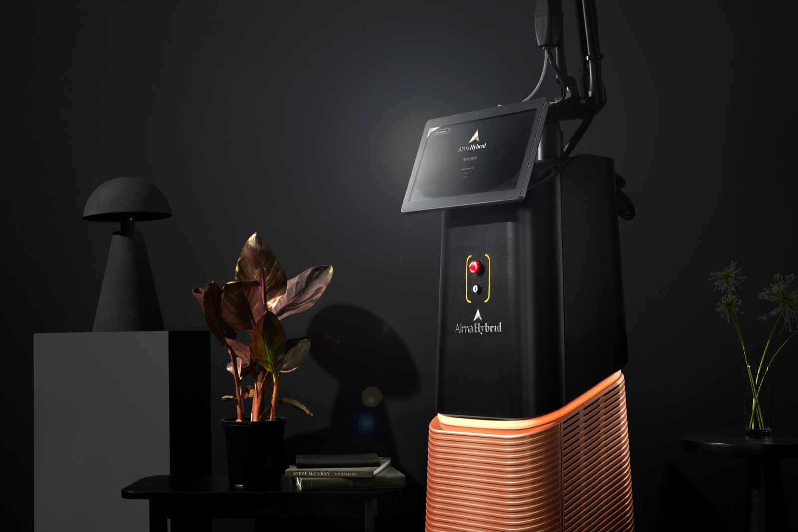 The Alma Hybrid laser, black with a glowing copper base, its touchscreen showing the Alma Hybrid welcome screen