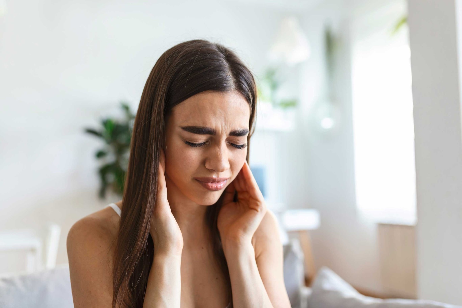 A woman with her eyes closed, pressing both hands to the sides of her jaw in discomfort
